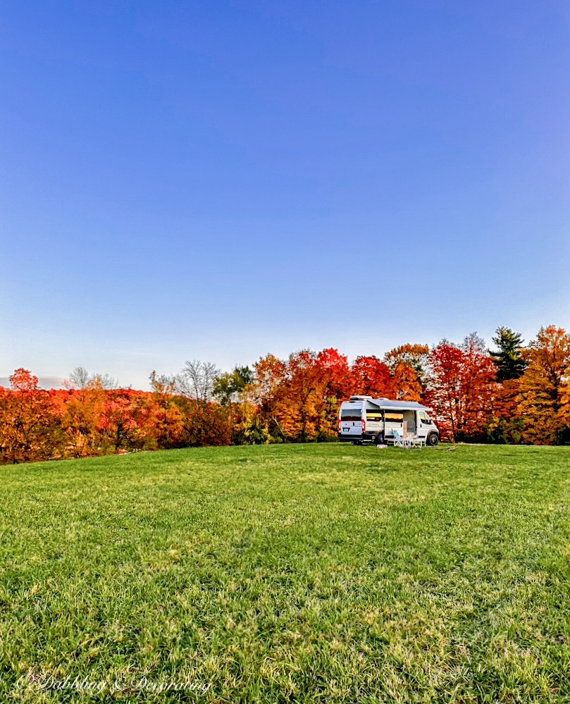 White RV in a field of green grass on top of a mountain in peak fall foliage during a Vermont fall weekend.