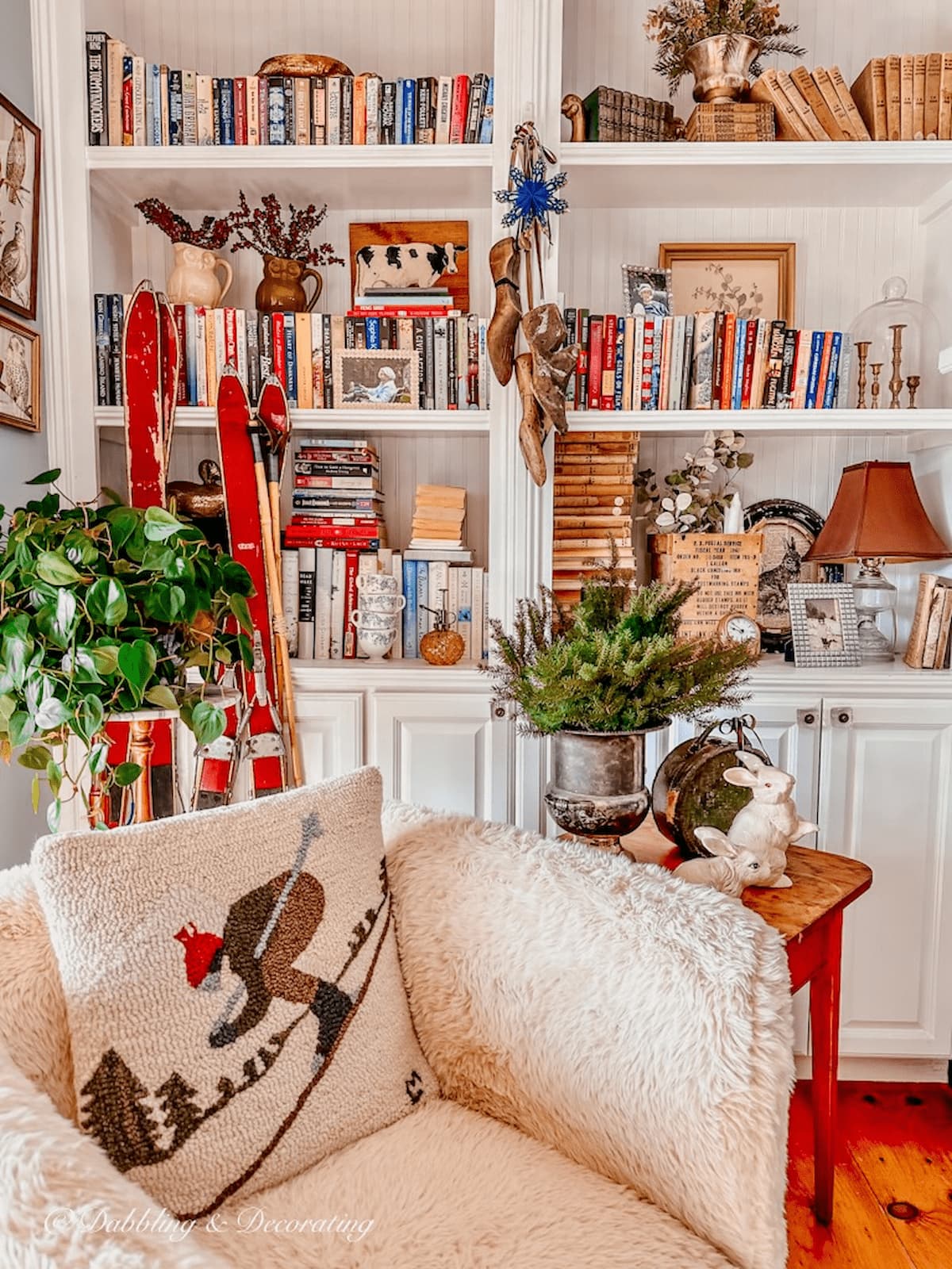 Cozy corner book nook with sheepskin chair, side table plants, and hanging decorative wood spindles on bookshelving. Vintage Skis for Decoration.