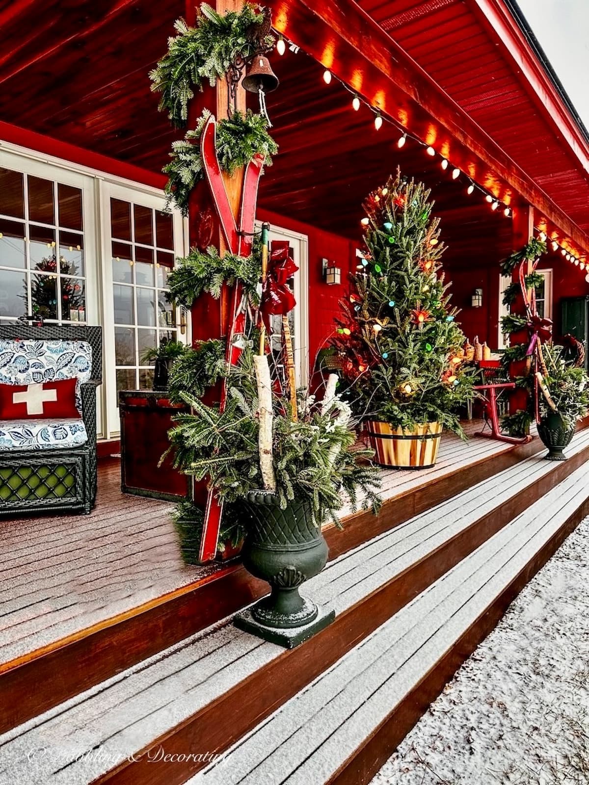 Christmas decorations on Apres ski theme porch in the mountains with plastic urn planters with evergreens and birch logs. New England vintage Christmas decorating ideas.