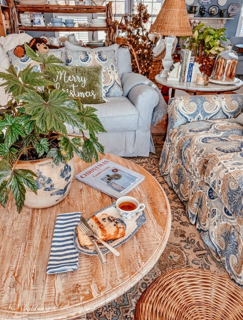 Blue and white cozy styled living room with Johnson Brother's tea and toast vintage dish with blueberry cake and tea, Christmas with Country Living Book ad green plant in crock on round coffee table.