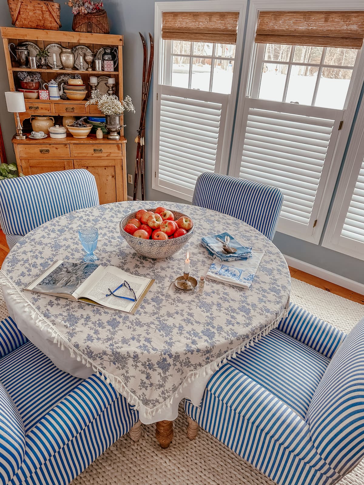 Blue and white dining room table with vintage hutch and three large windows with no drill woven shades and blinds.