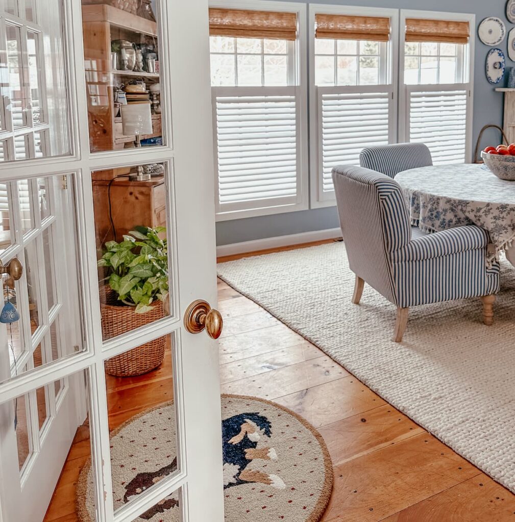 French door opening up into dining room with blue and white chairs, white rug and windows with bamboo shades and blinds and wood flooring.