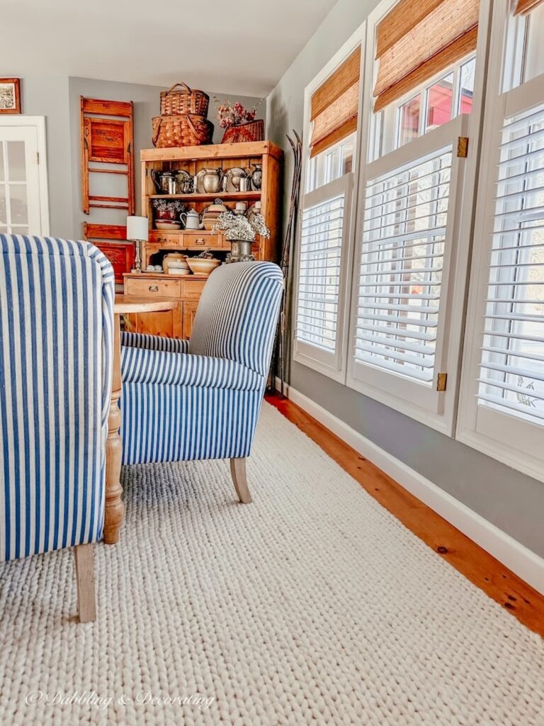 Dining room with three windows of natural cordless blinds with blue and white striped chairs, white braided rug and vintage hutch.