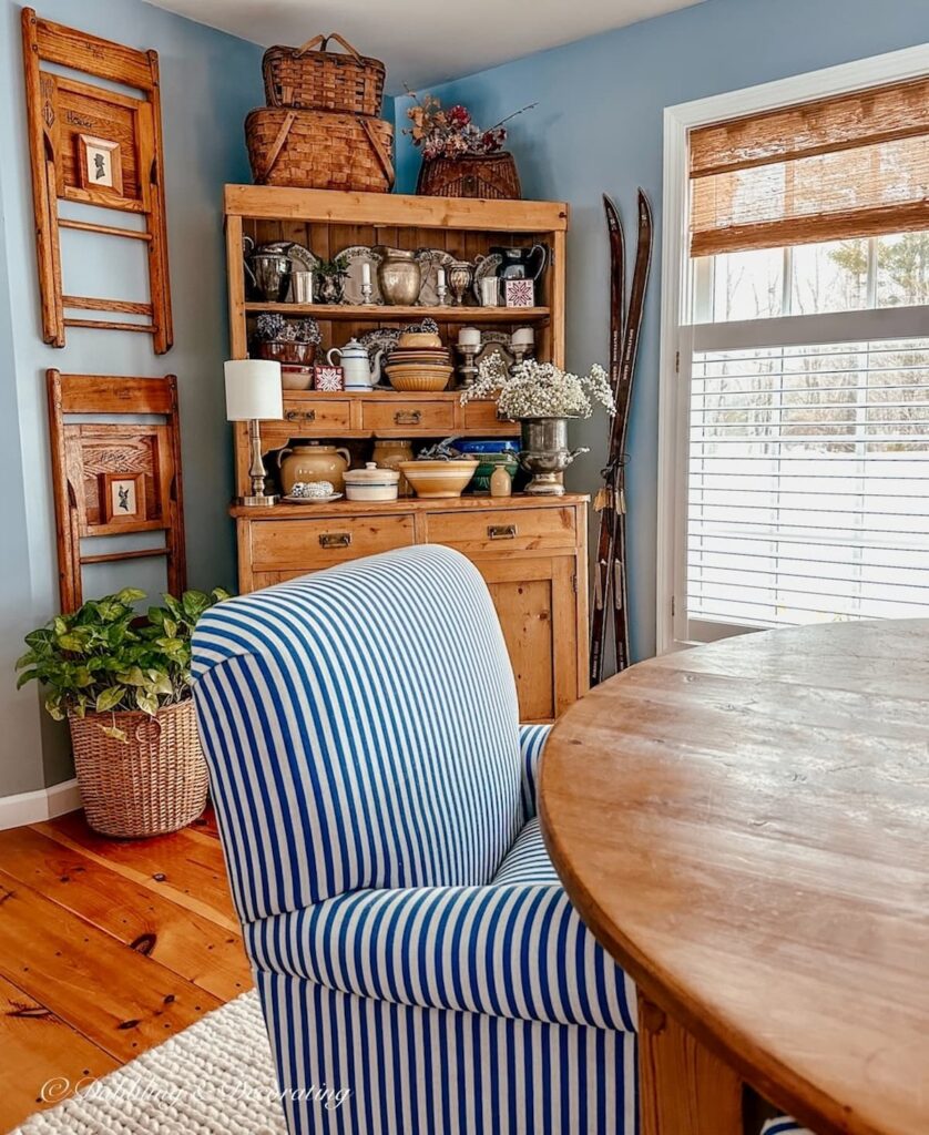 Vintage style dining room with blue and white striped chair at table with vintage wall decor chairs hanging on wall with small silhouette prints next to hutch.