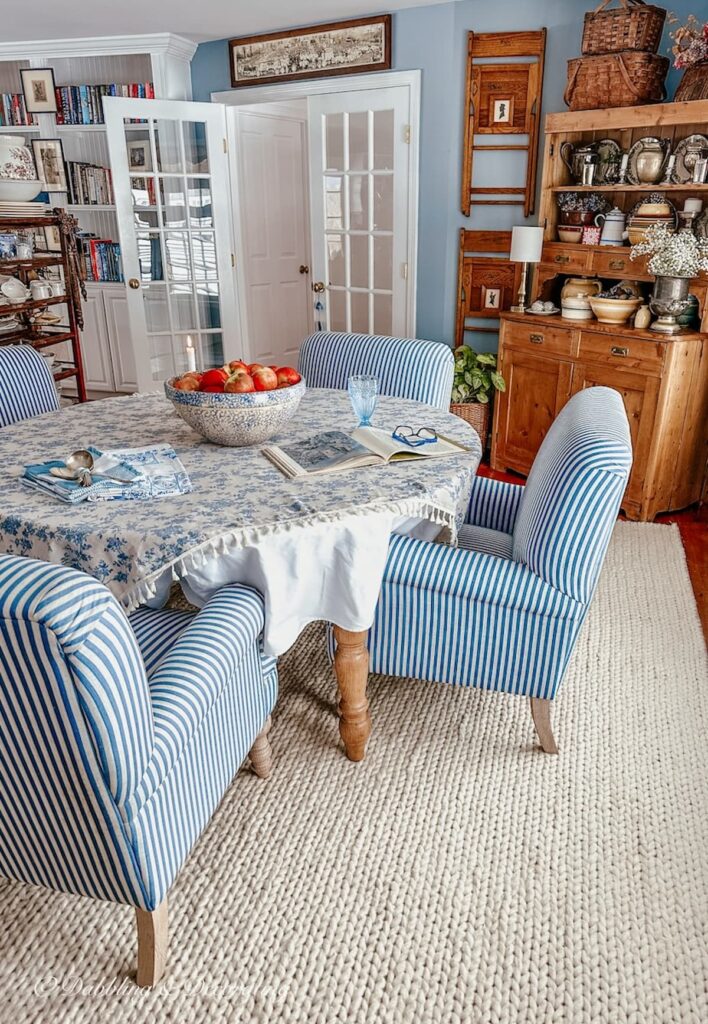 Vintage style dining room with blue and white chairs around round table on white rug with vintage wall decor and hutch. Eclectic Decorating Style