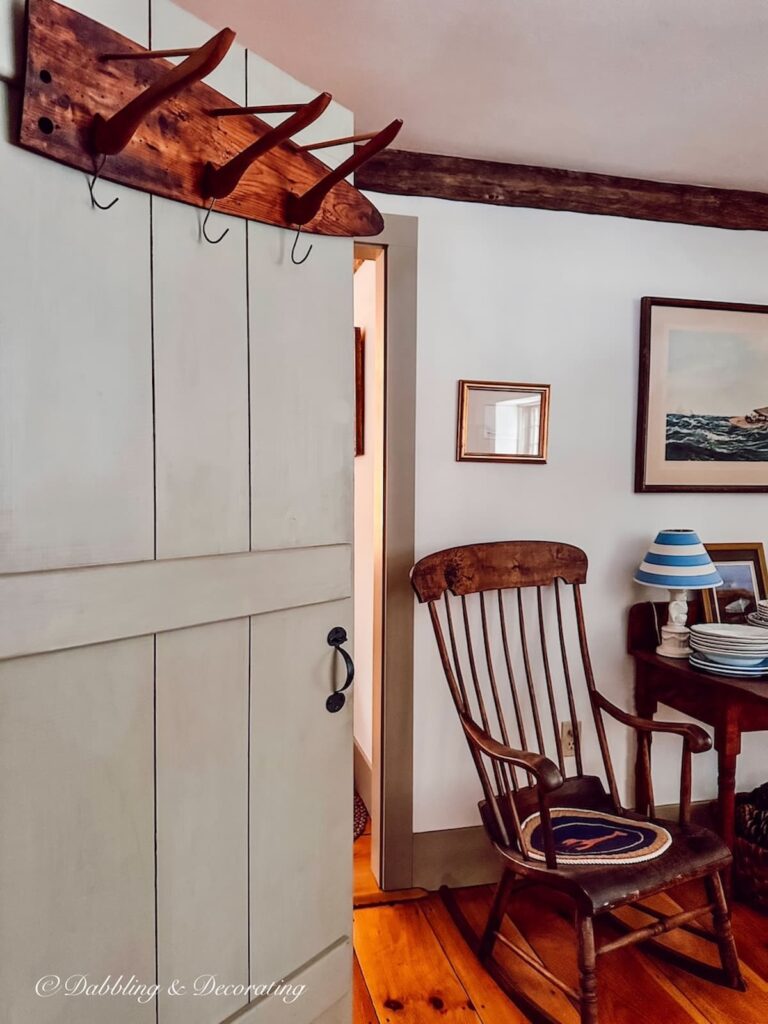 Wooden DIY coat rack hanging on antique home's pantry open door with rocking chair and vintage coastal decor.