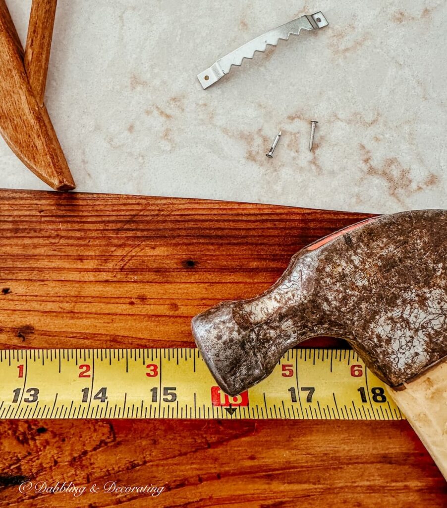 Hammer, tape measure, board and saw booth screw with two screws on counter.