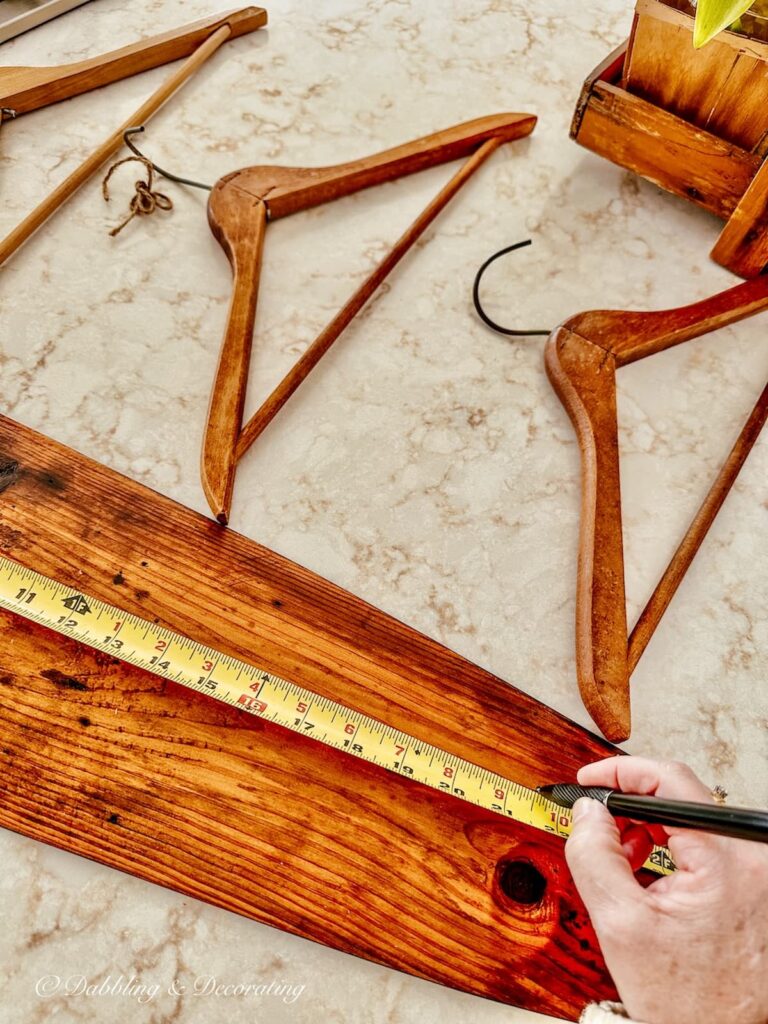 Antique trapper's board with person measuring it and marking it for a DIY coat rack.