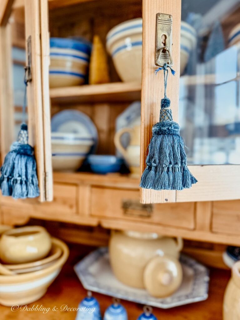 Blue tassels hanging from vintage pine hutch doors filled with vintage yellowware.