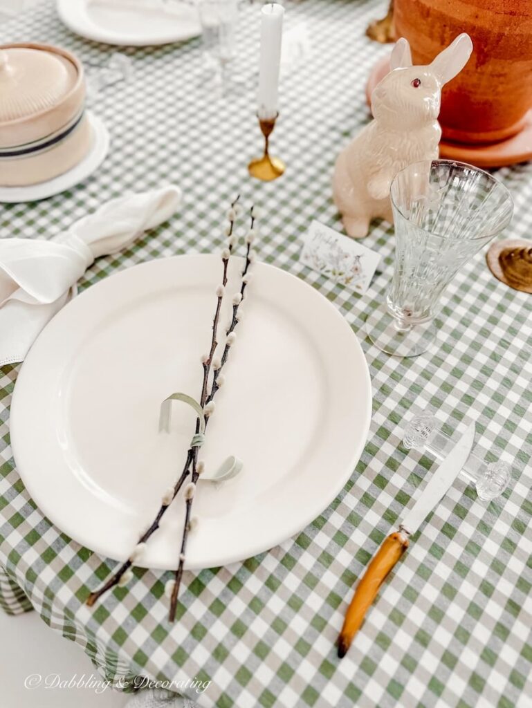 White dinner plate on green gingham table with pussy willows and vintage champagne flute.