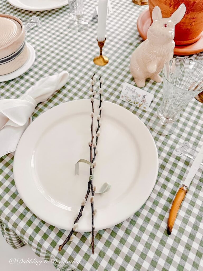 White Dinner plate on green gingham tablecloth with pussy willow branches tied with a ribbon on Easter Tablescape.