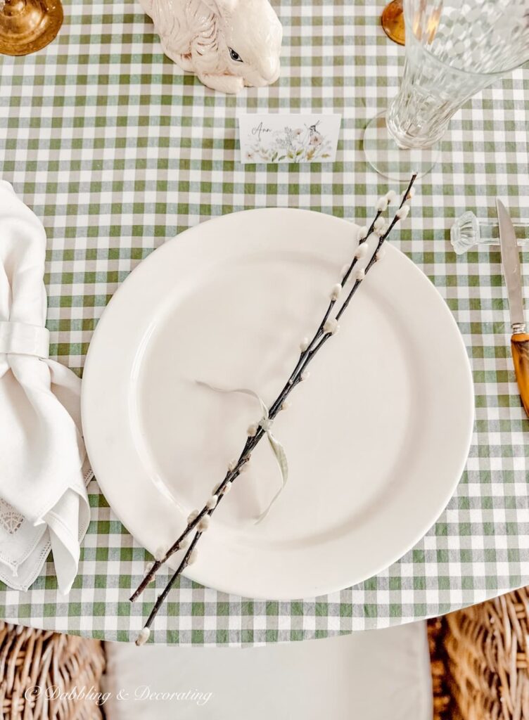 White vintage dinner plate with pussy willow branches tied with a bow on a table with a green and white gingham tablecloth.