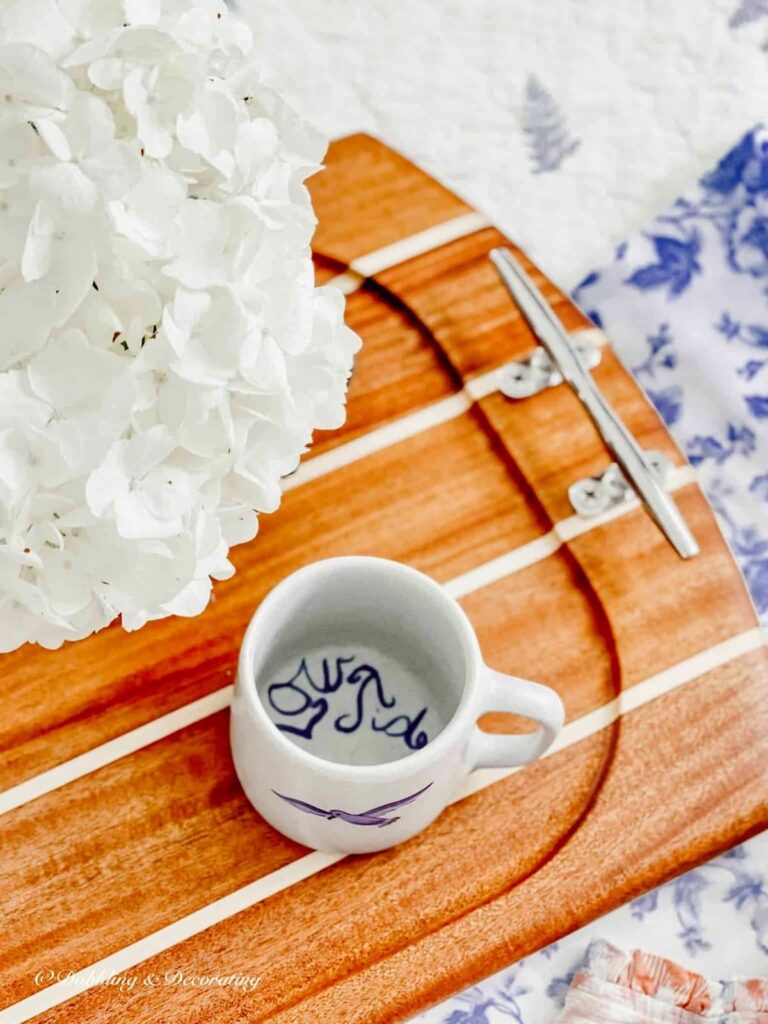 Wooden nautical serving tray with Low Tide mug and white hydrangeas on bed.