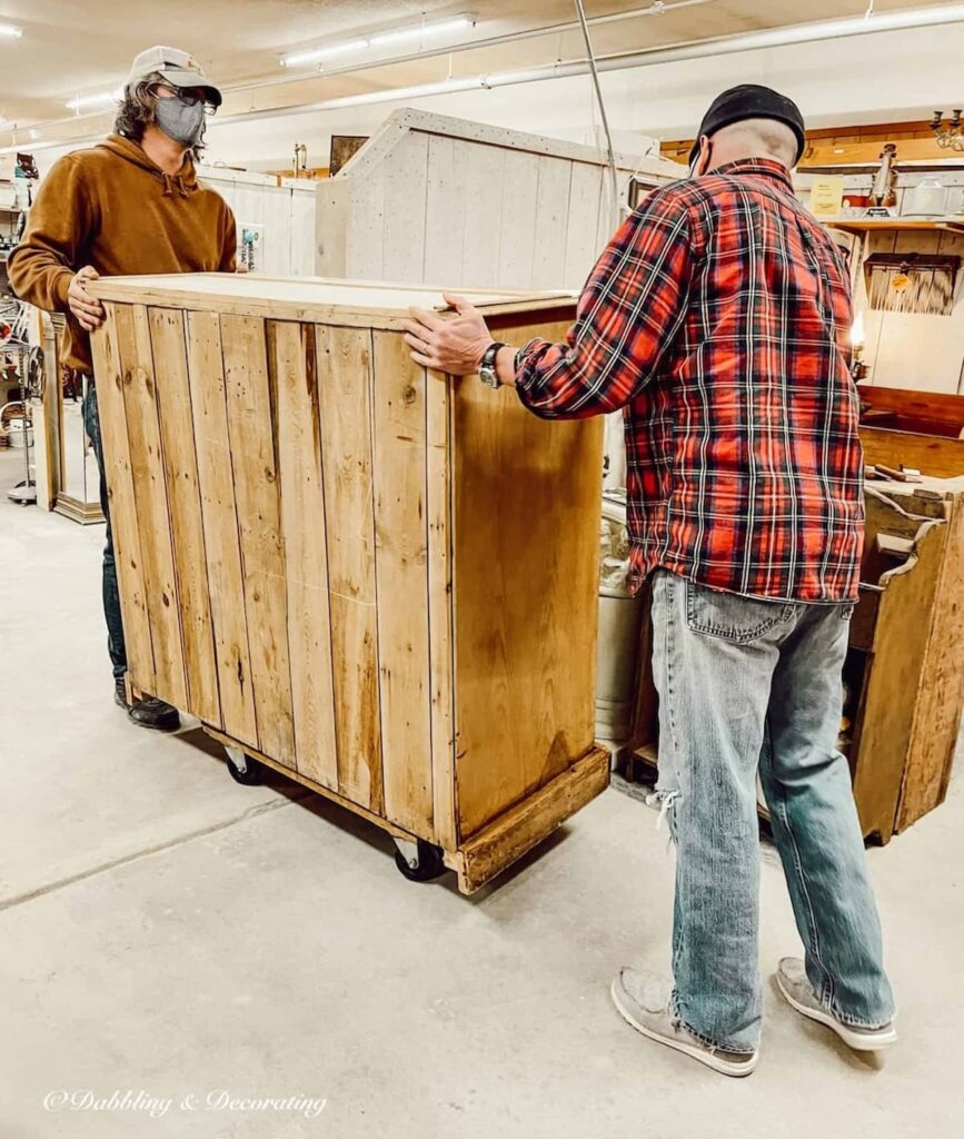 Two men rolling large antique hutch out of antique store.