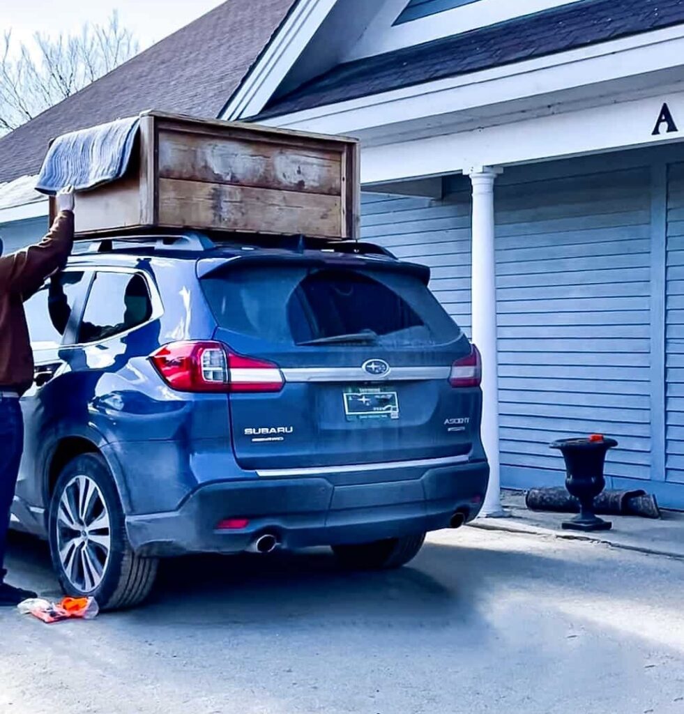 Blue Subaru with vintage hutch loaded on top at antique store.
