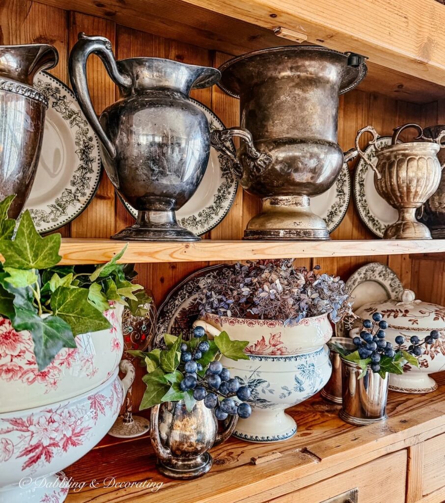 Collection of silver tin vintage pitchers in pine hutch.