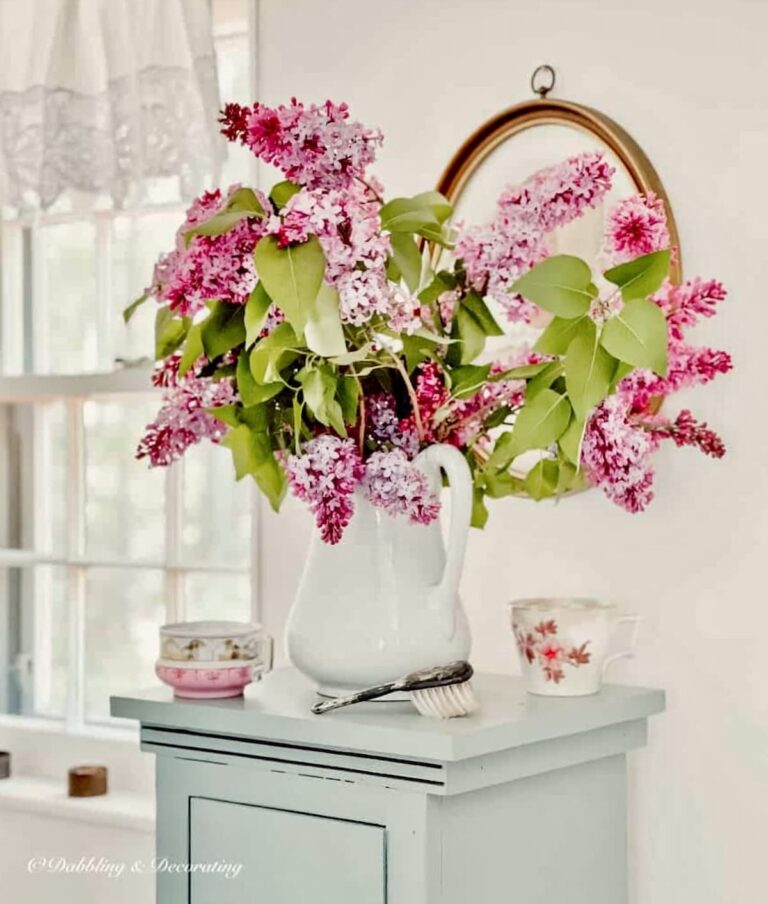 Lilac flower bouquet in white ironstone pitcher styled in vintage bathroom.