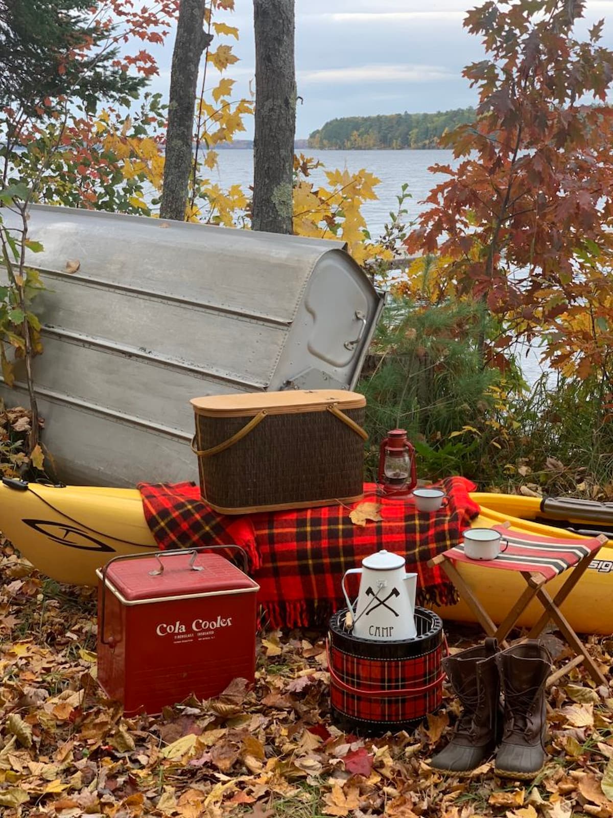 Camp Lakeside picnic with red plaid blanket, vintage red cooler, overturned row boat and vintage picnic basket.