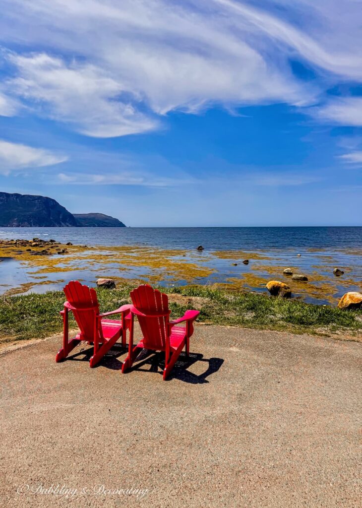 Two red Adirondack chairs overlooking the Atlantic Newfoundland rocky coast.