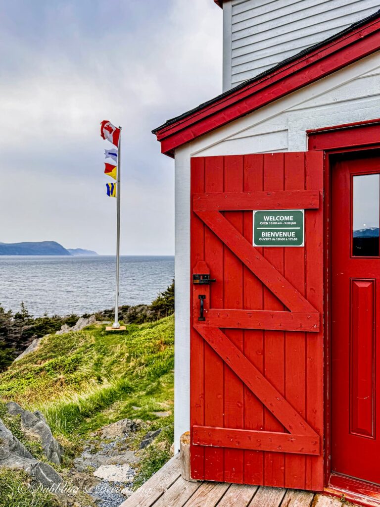 Lobster Cove Lighthouse Red door and flag pole overlooking Atlantic Ocean antiquing in Newfoundland.