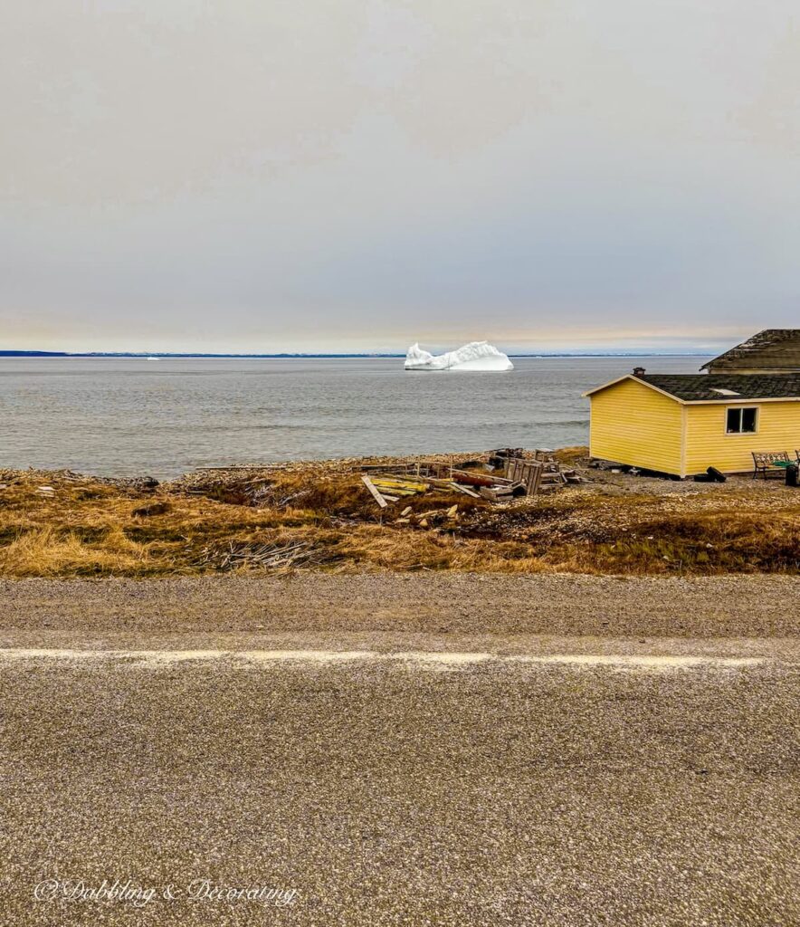 Large iceburg in the Atlantic and yellow house on iceberg alley coastal drive.