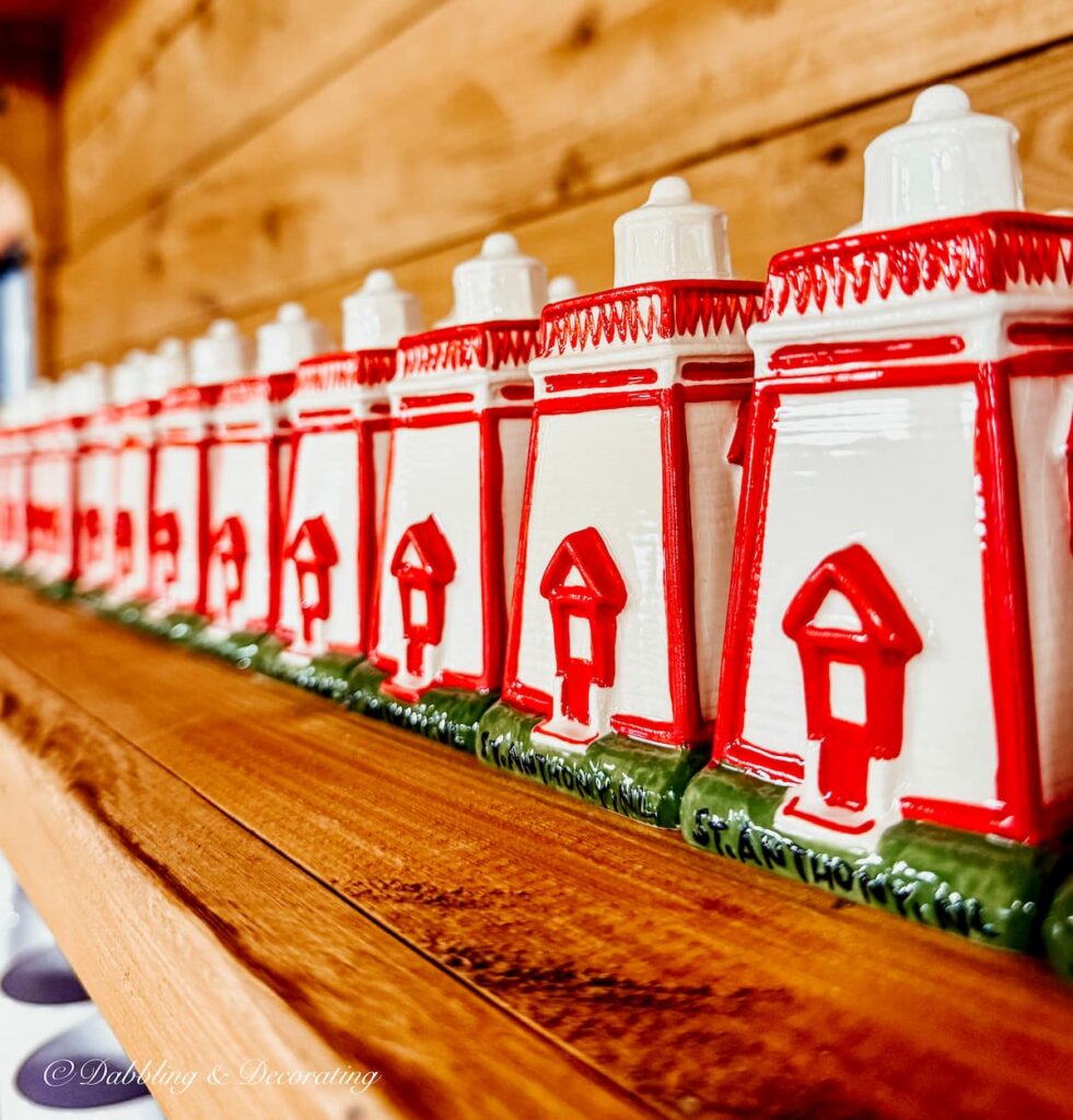 A line of small red and white lighthouse salt and pepper shakers on shelf.