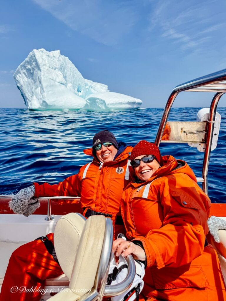 Ann and Steve in boat in the Atlantic in front of Iceberg in Newfoundland with flotation suites on.