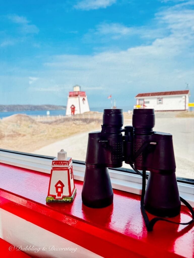 Binoculars with lighthouse salt shaker on red windowsill overlooking lighthouse.