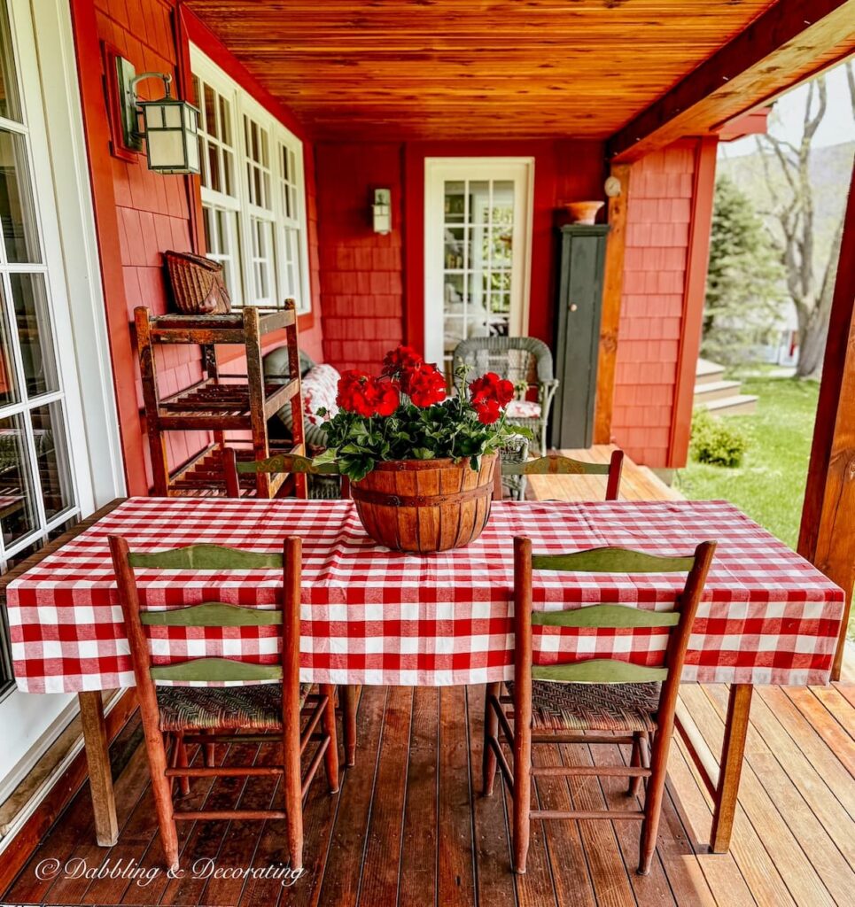 Vintage porch decor for spring with gingham red and white tablecloth with wooden basket of red geraniums in the mountains.