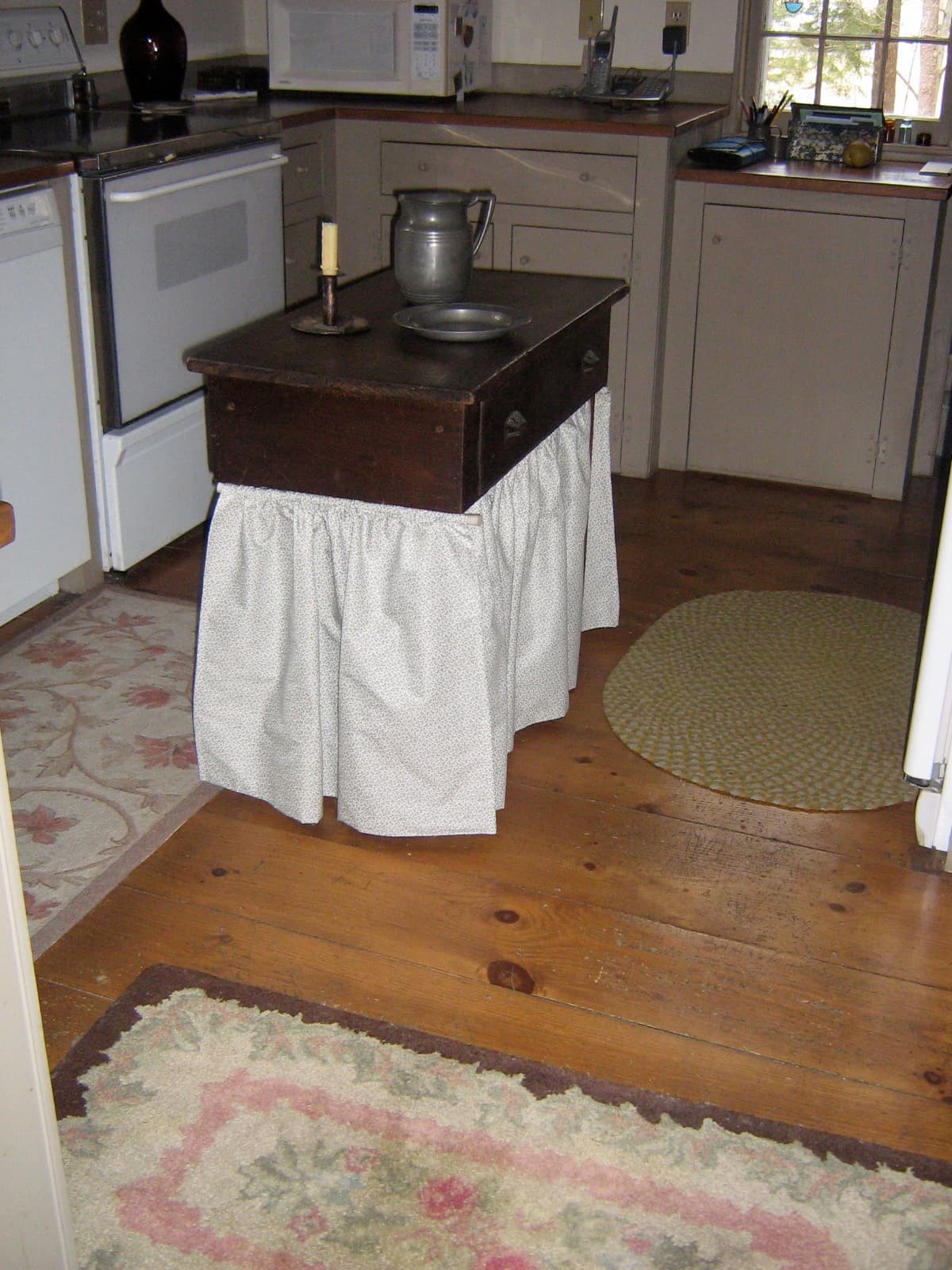 Antique kitchen center small table with pewter and handmade curtains wrapped around the bottom in country kitchen.