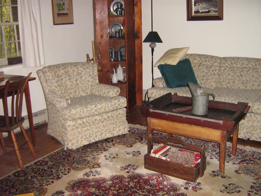 Antique living room decor with hutch filled with pewter and antique rug in Maine home.