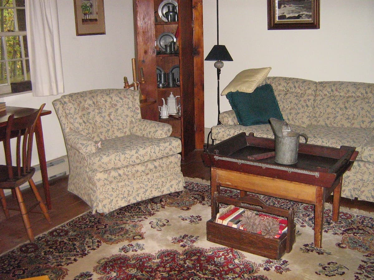 Antique living room decor with hutch filled with pewter and antique rug in Maine home.