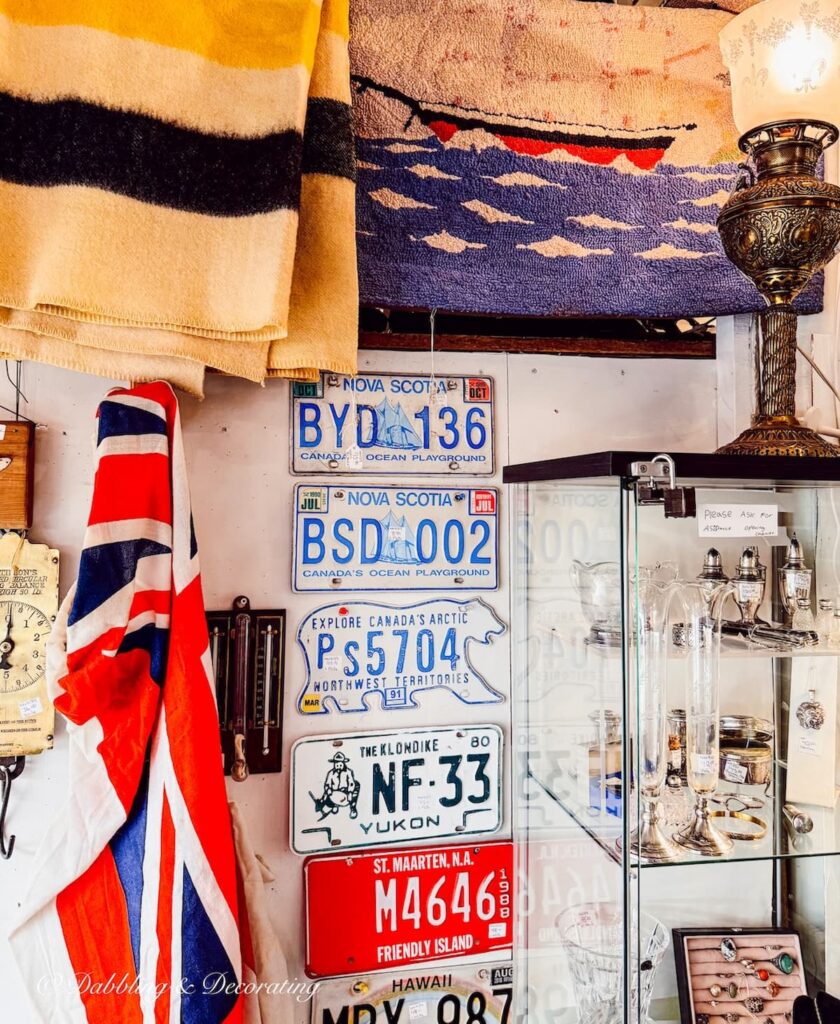 Red, white, and blue Nova Scotia license plates in antique stores with flags and hooked rugs.