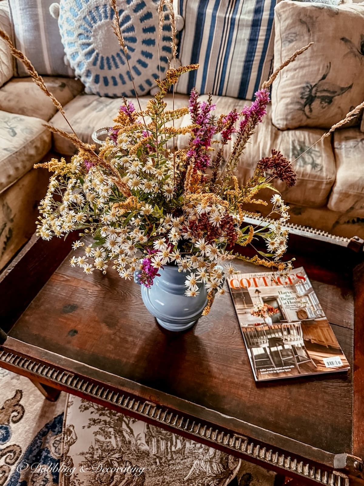 fall foraged weed flower arrangement in vintage blue vase on antique coffee table in living room with a Cottages and Bungalows Magazine.