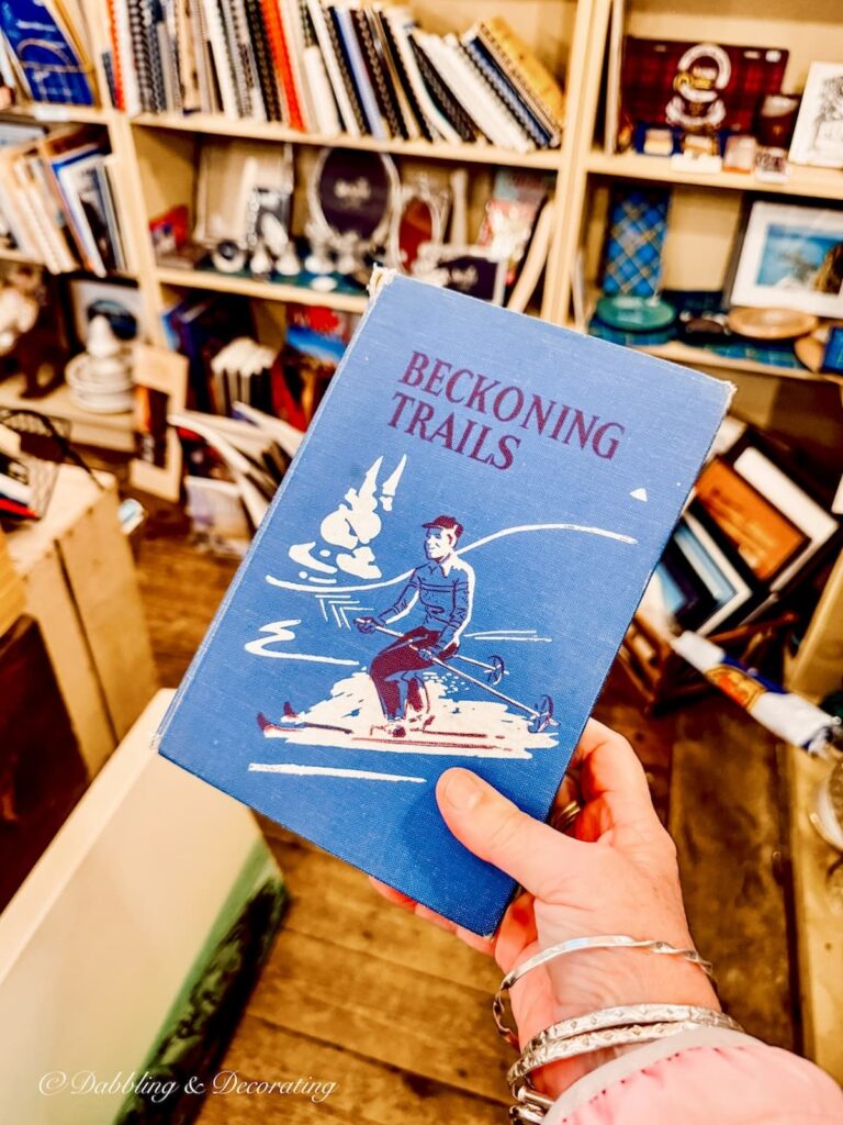 Blue Beckoning Trails book with skier in antique store in hand.