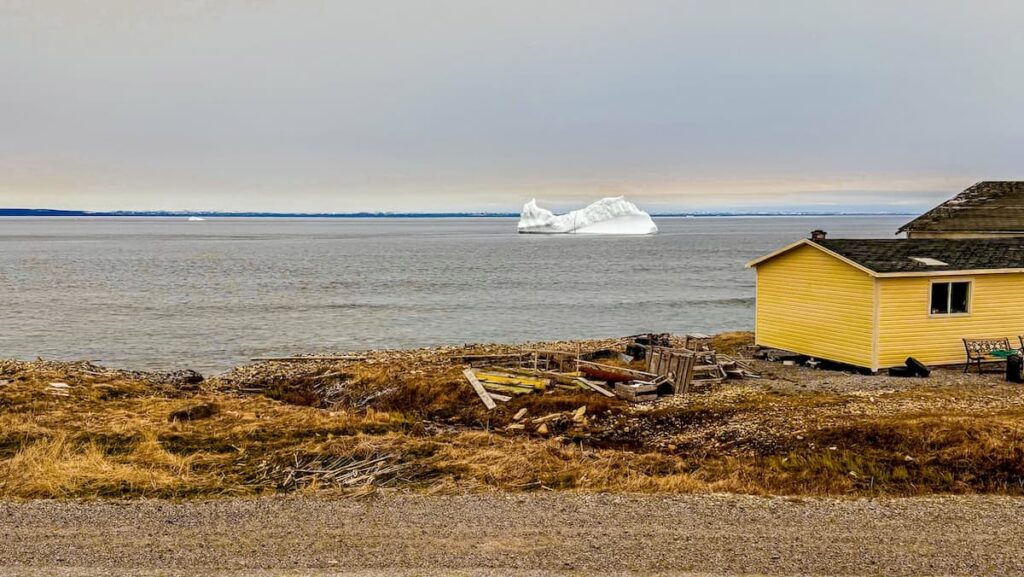 Iceberg floating on the ocean scenery in Newfoundland net to a yellow house.