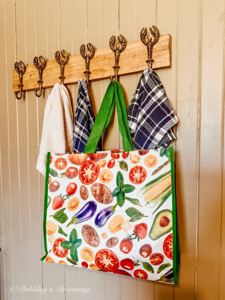 Lobster coat rack with colorful bag and dish towels hanging from it in coastal cottage decor ideas.