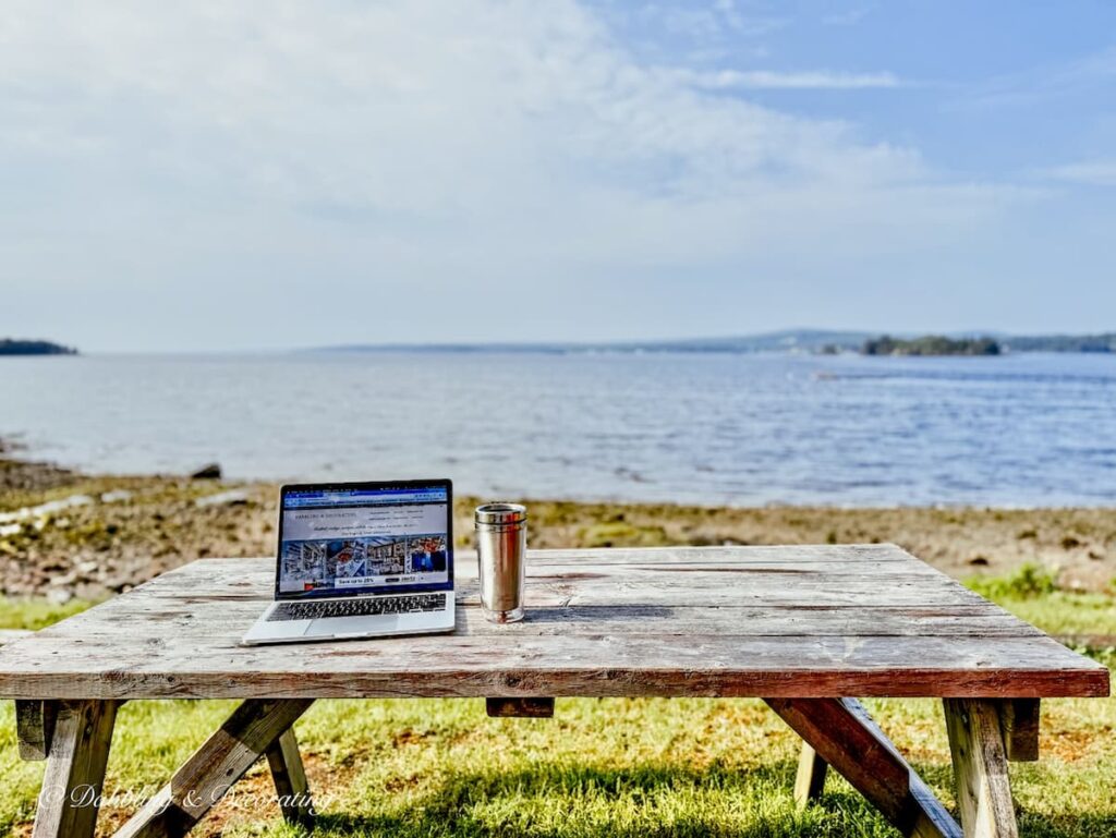 Laptop and travel coffee mug on picnic table at the Bay of Fundy.