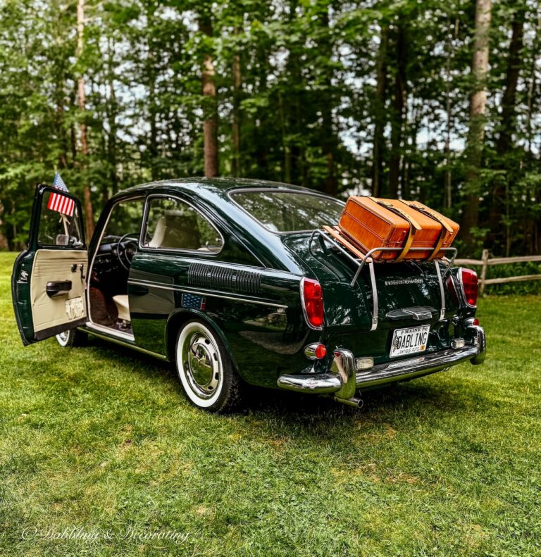 Green VW 1968 Fastback with luggage rack, suitcase and American flag on antenna for 4th of July stying in backyard.