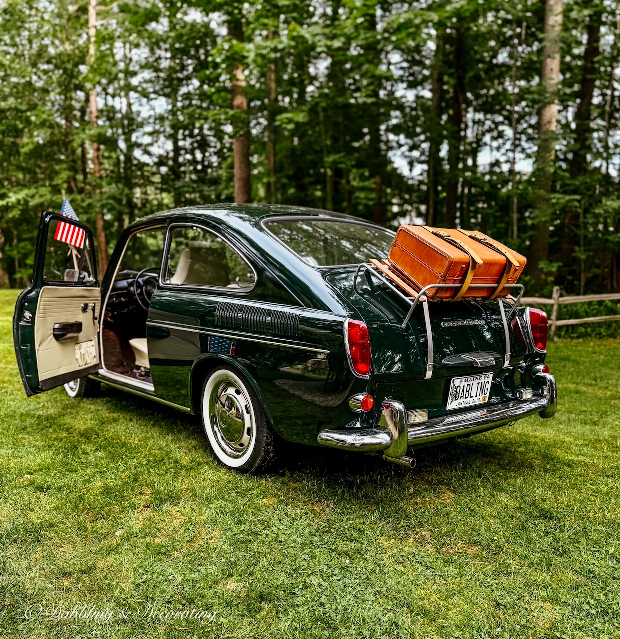 Green VW 1968 Fastback with luggage rack, suitcase and American flag on antenna for 4th of July stying in backyard.