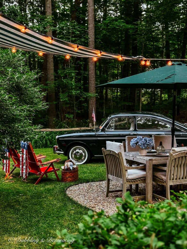 Outdoor backyard with teak table patio set up with Sun Shade Sail awning with white lights and old car for summer decor in the evening.