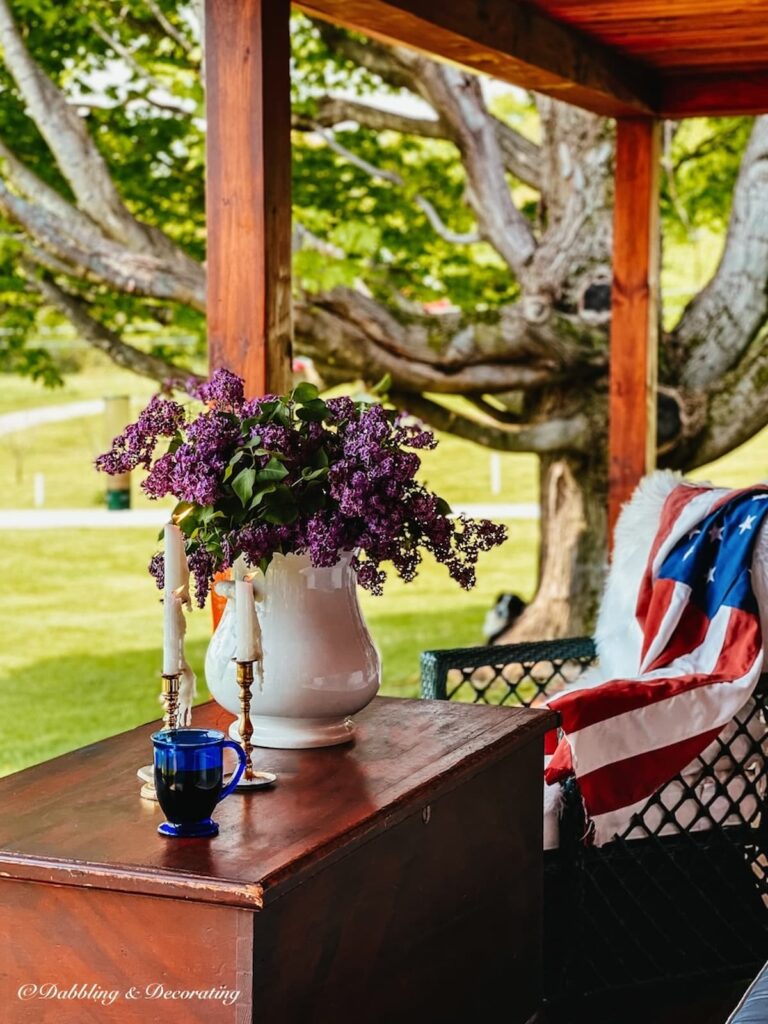 Lilac bouquet in an old vintage white grub pot styled with Patriotic details on a covered porch.