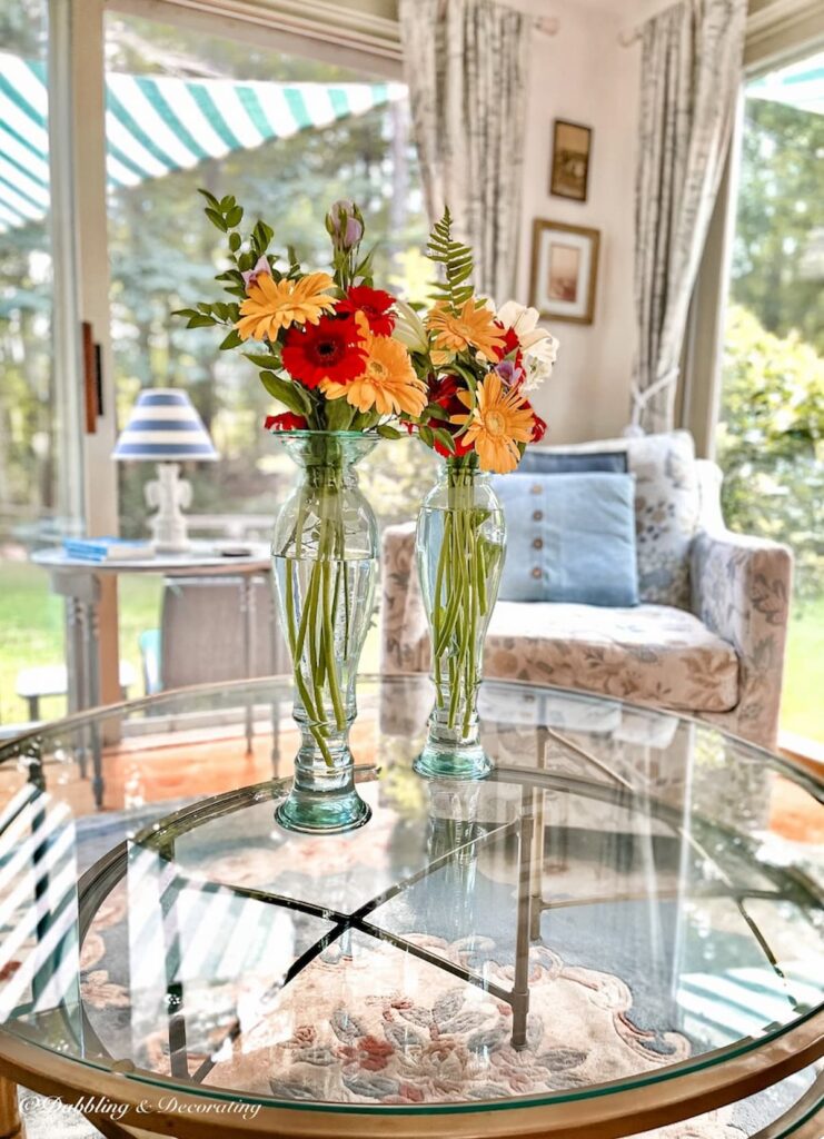 Two tall vases/candle sticks with colorful flowers on sunroom glass coffee table.