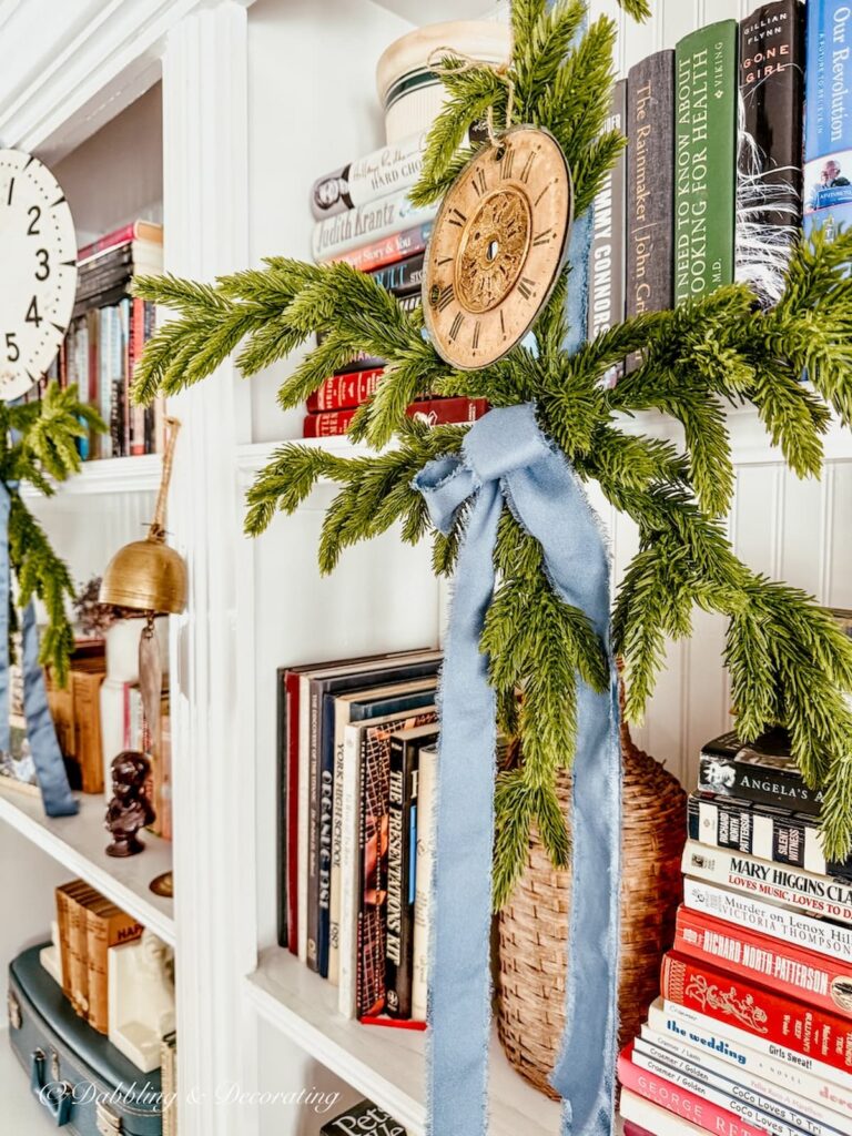 Vintage bookshelf decor for New Years with vintage clock faces tied to snowflakes with blue ribbon.