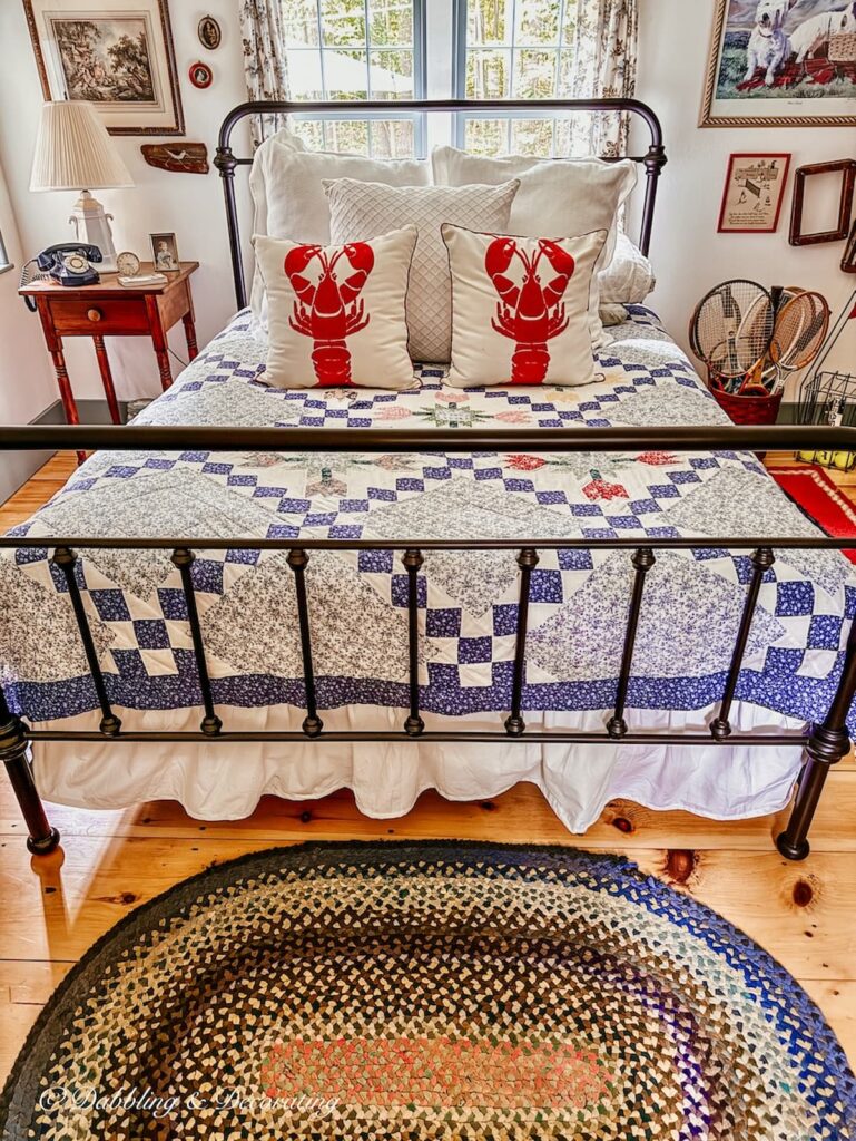 Vintage coastal style bedroom with wrought iron bed, vintage quilt, braided rug and two lobster pillows.
