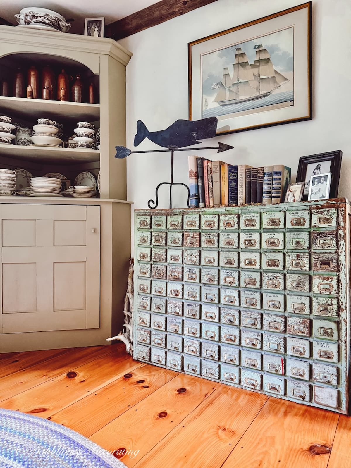 Antique apothecary cabinet with wrought iron whale weathervane in dining room with corner hutch filled with antique collections in New England home.