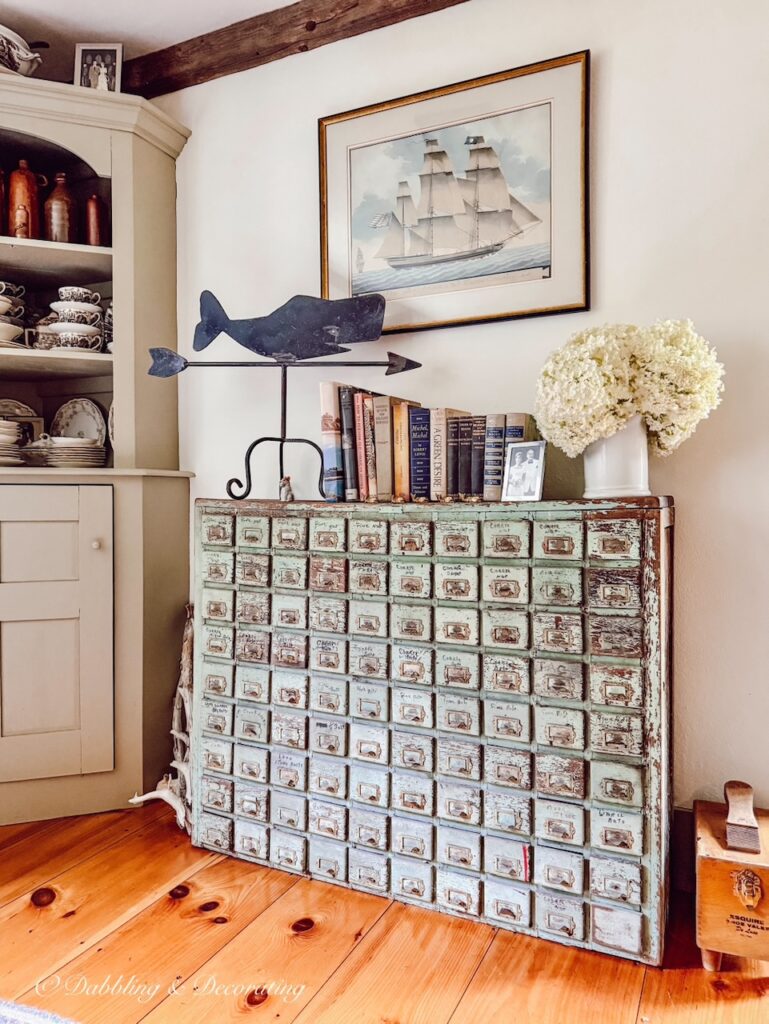 Antique apothecary cabinet with whale wrought iron weathervane, nautical sailboat photo and vintage books in dining room. Eclectic Decorating Style Ideas.