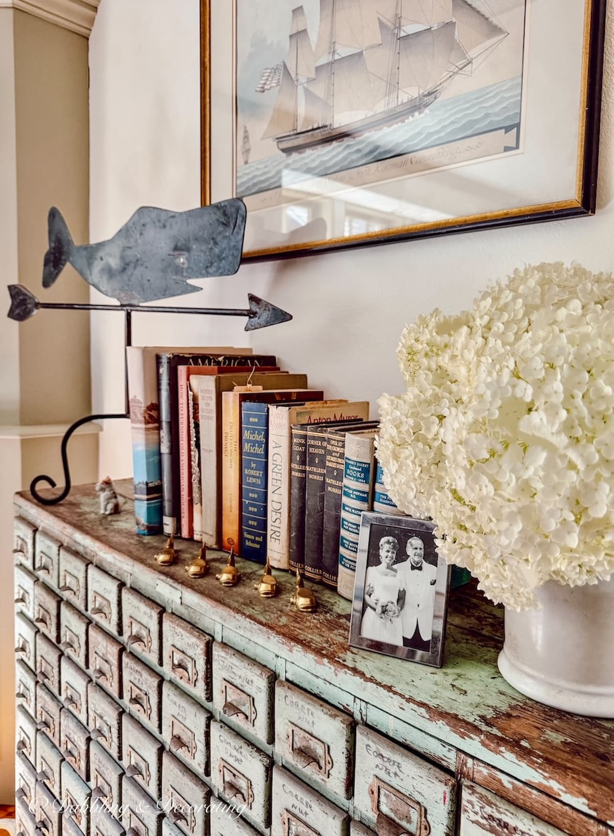 Antique wrought iron whale weathervane on antique apothecary in vintage coastal decor style home in Maine. Small framed silver picture of father and daughter.