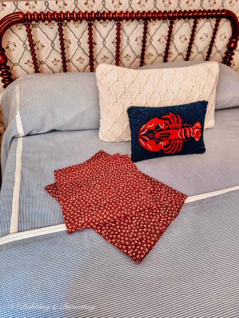 Antique Jenny Lind bed with Searsucker bedding, lobster pillow and handmade red floral curtains in coastal decor room.