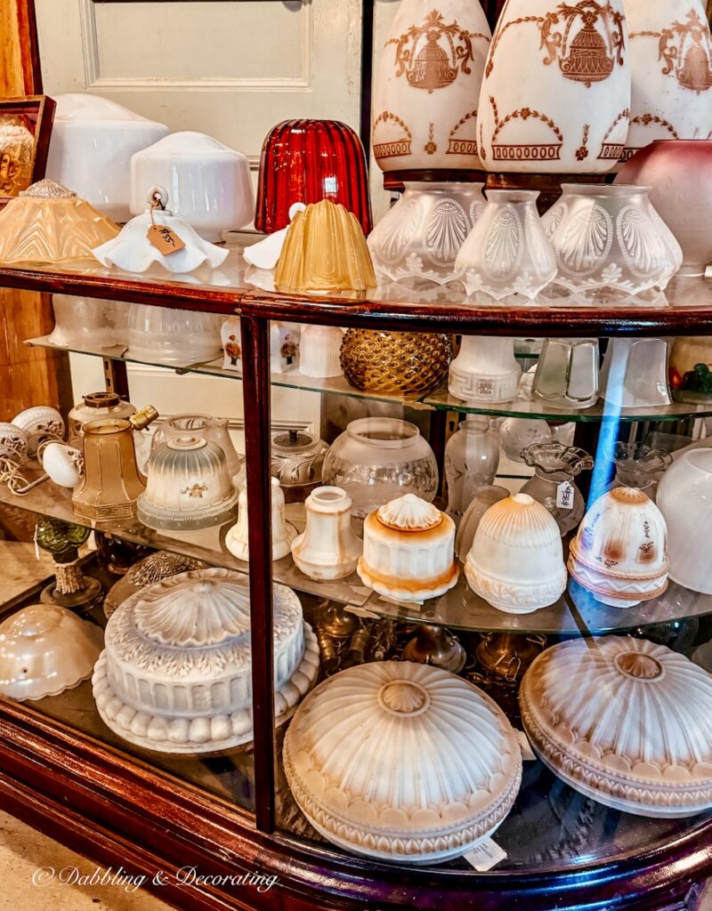 Antique glass lamp shades displayed in a glass cabinet at store.